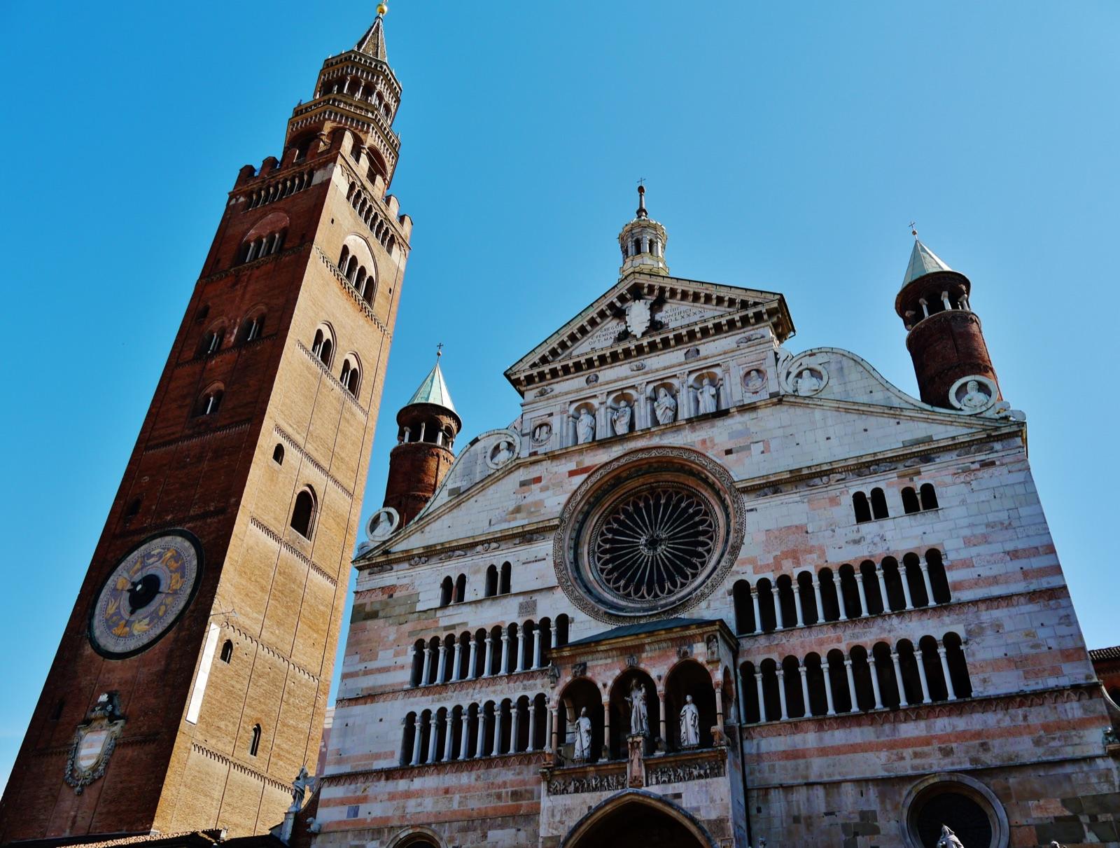 Il Torrazzo e la facciata del Duomo di Cremona sotto un cielo azzurro