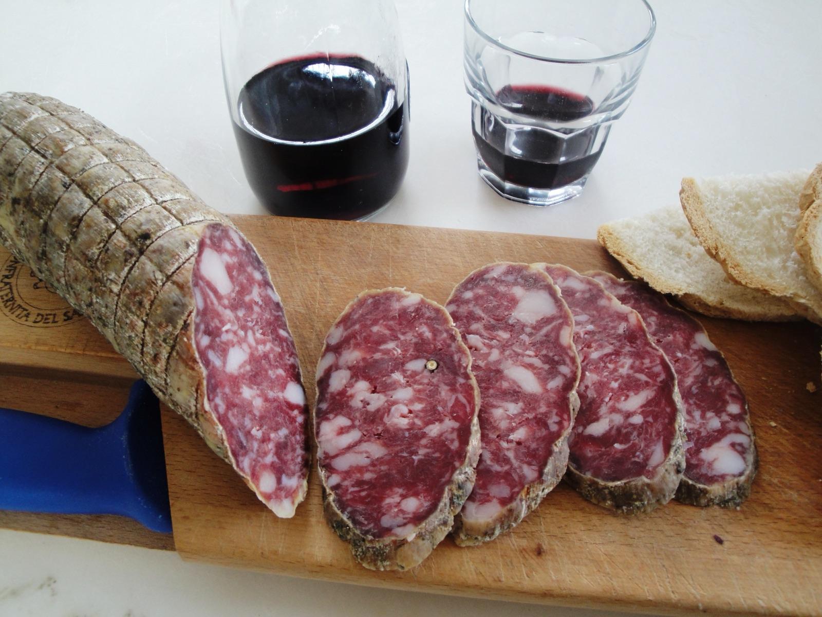 Salame di Varzi affettato su un tagliere con pane e un bicchiere di vino rosso
