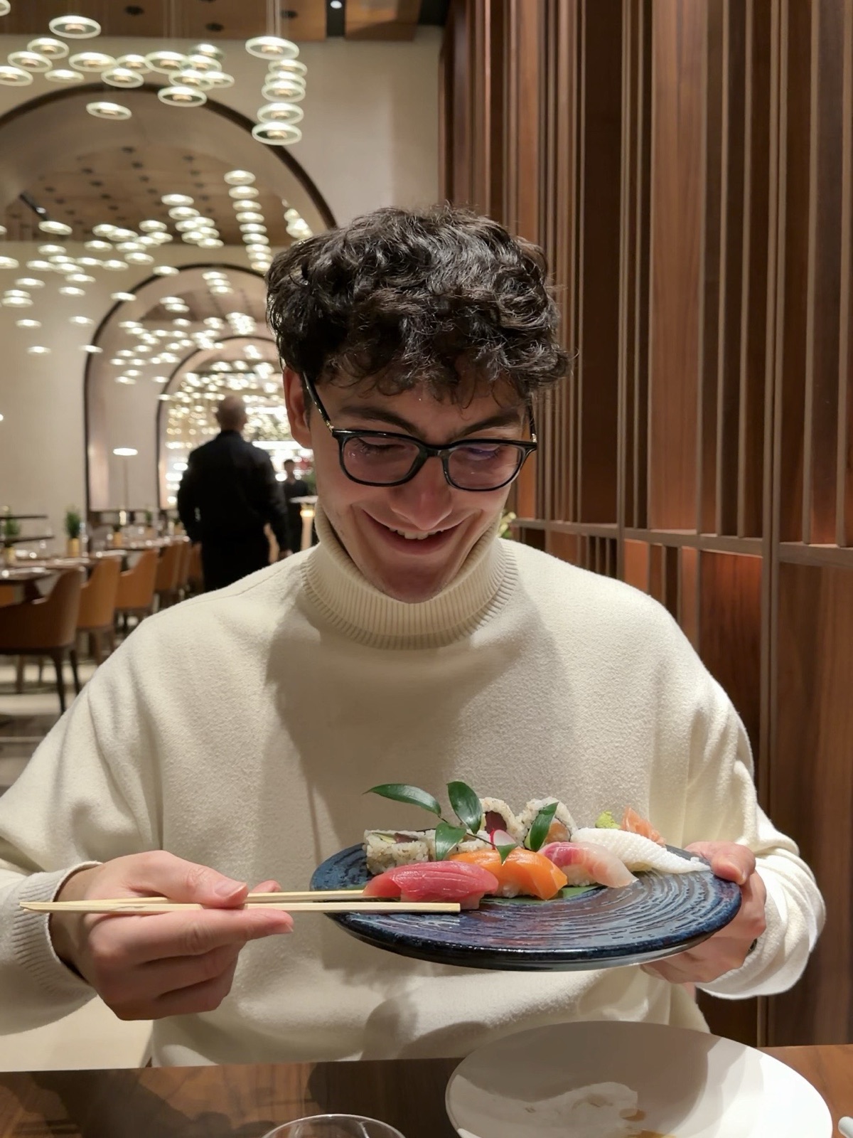 Gianmaria sorridente al tavolo di Izu a Milano con un piatto di nigiri e sashimi