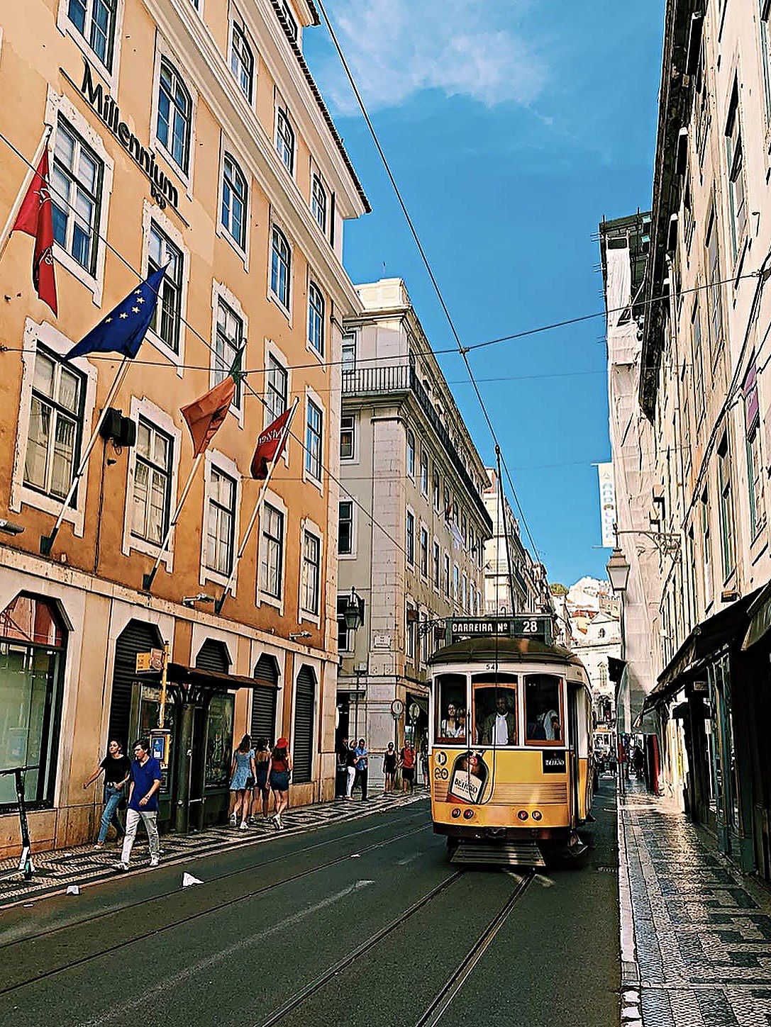 Il tram giallo numero 28 lungo una via della Baixa di Lisbona, tra i palazzi e le bandiere