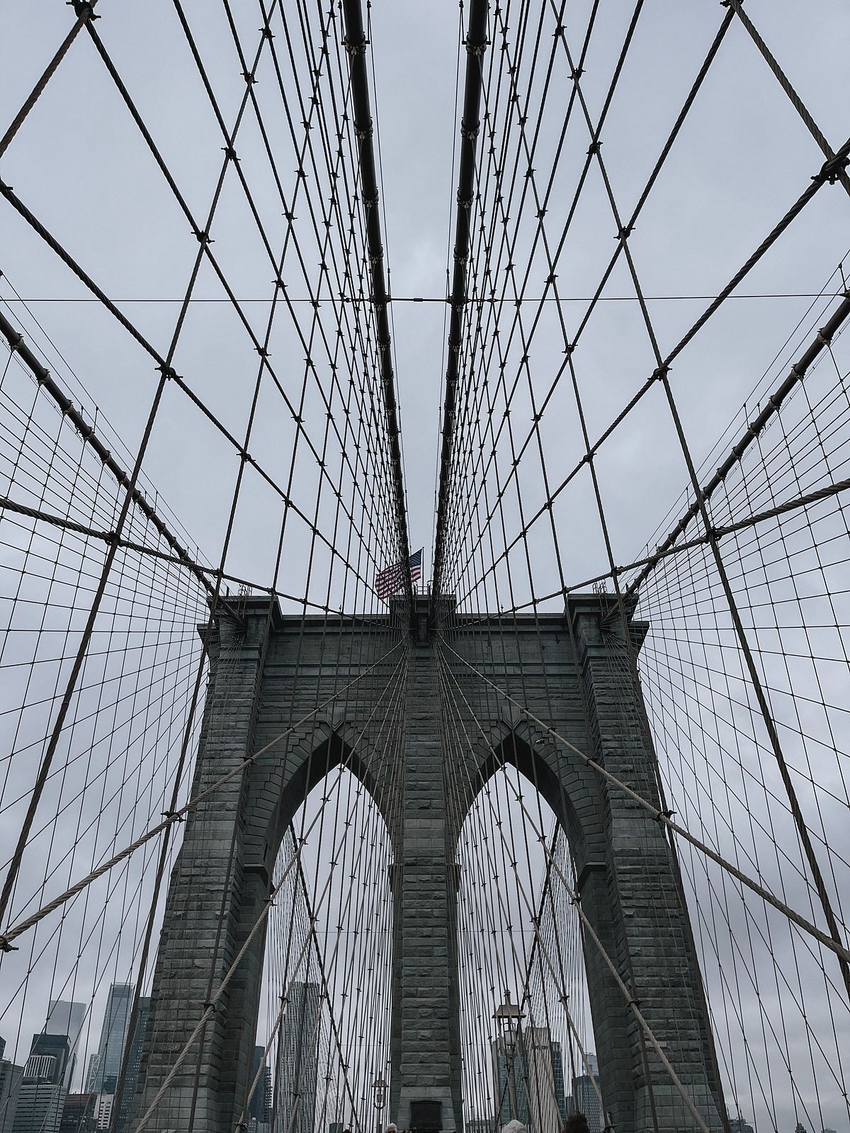 I piloni in pietra del Brooklyn Bridge con i cavi di acciaio e la bandiera americana