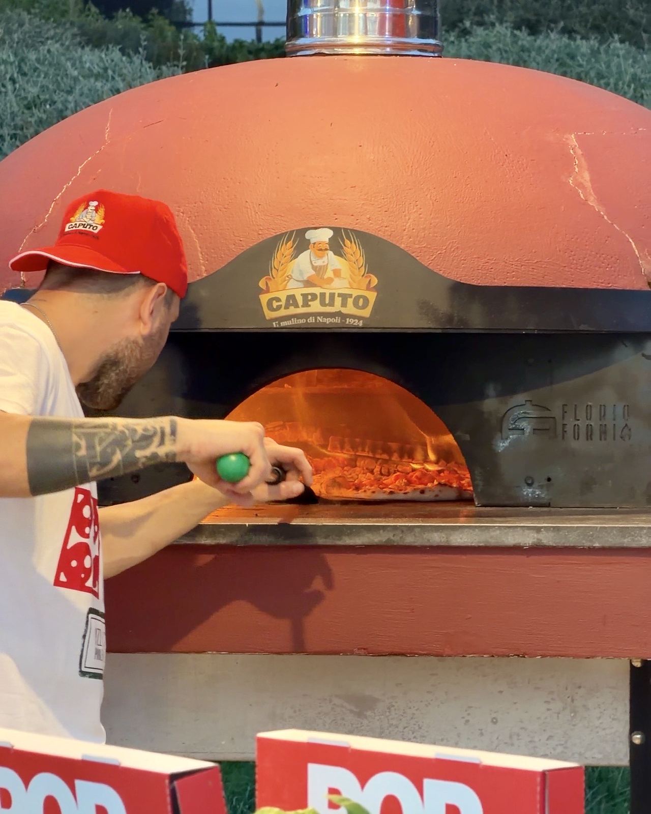 Pizzaiolo che inforna una pizza nel forno a legna di uno stand del Pizza Village di Milano