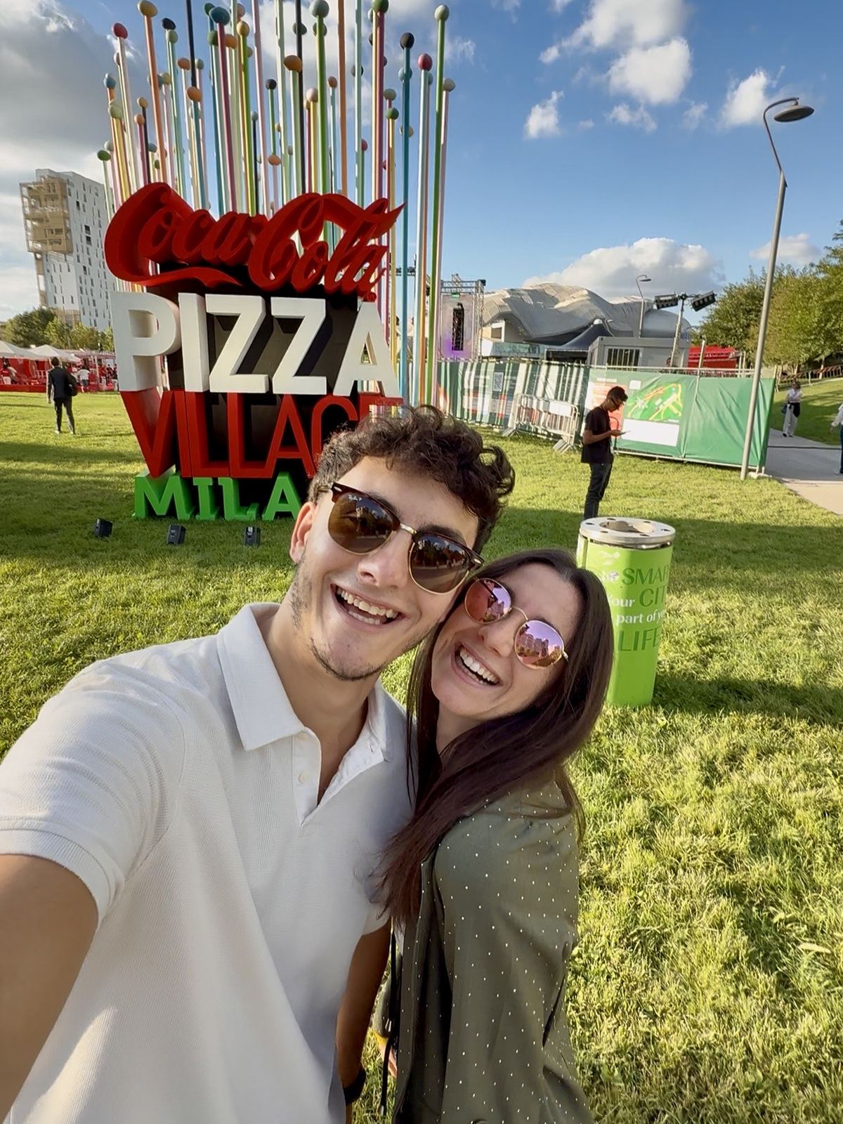 Ludovica e Gianmaria davanti all'insegna del Coca-Cola Pizza Village al Parco di CityLife a Milano