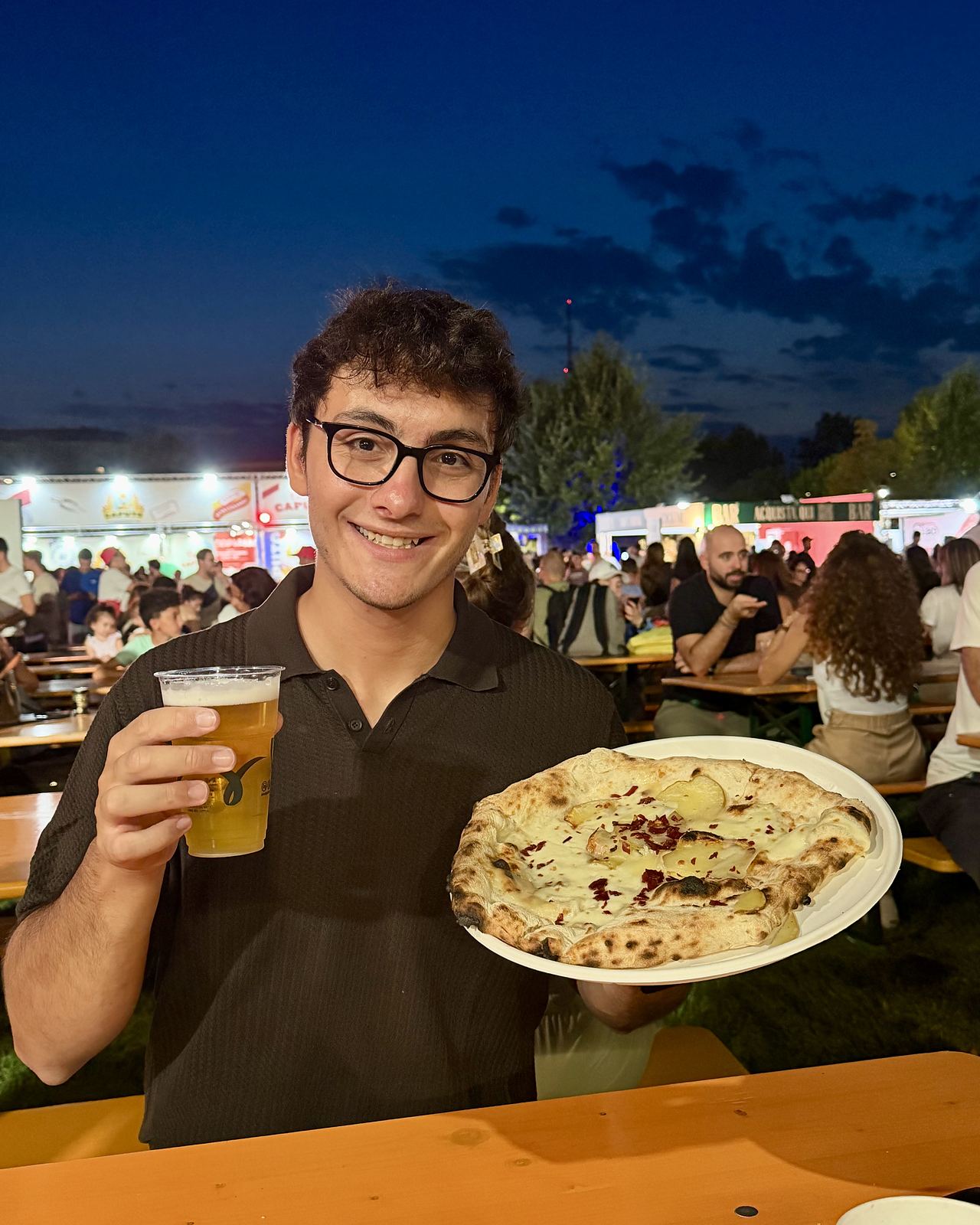 Gianmaria con una pizza e una birra in mano ai tavoli del Coca-Cola Pizza Village di Milano