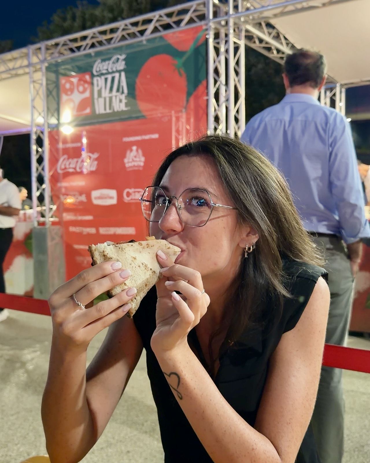 Ludovica mangia una pizza sandwich sotto l'insegna del Coca-Cola Pizza Village di Milano