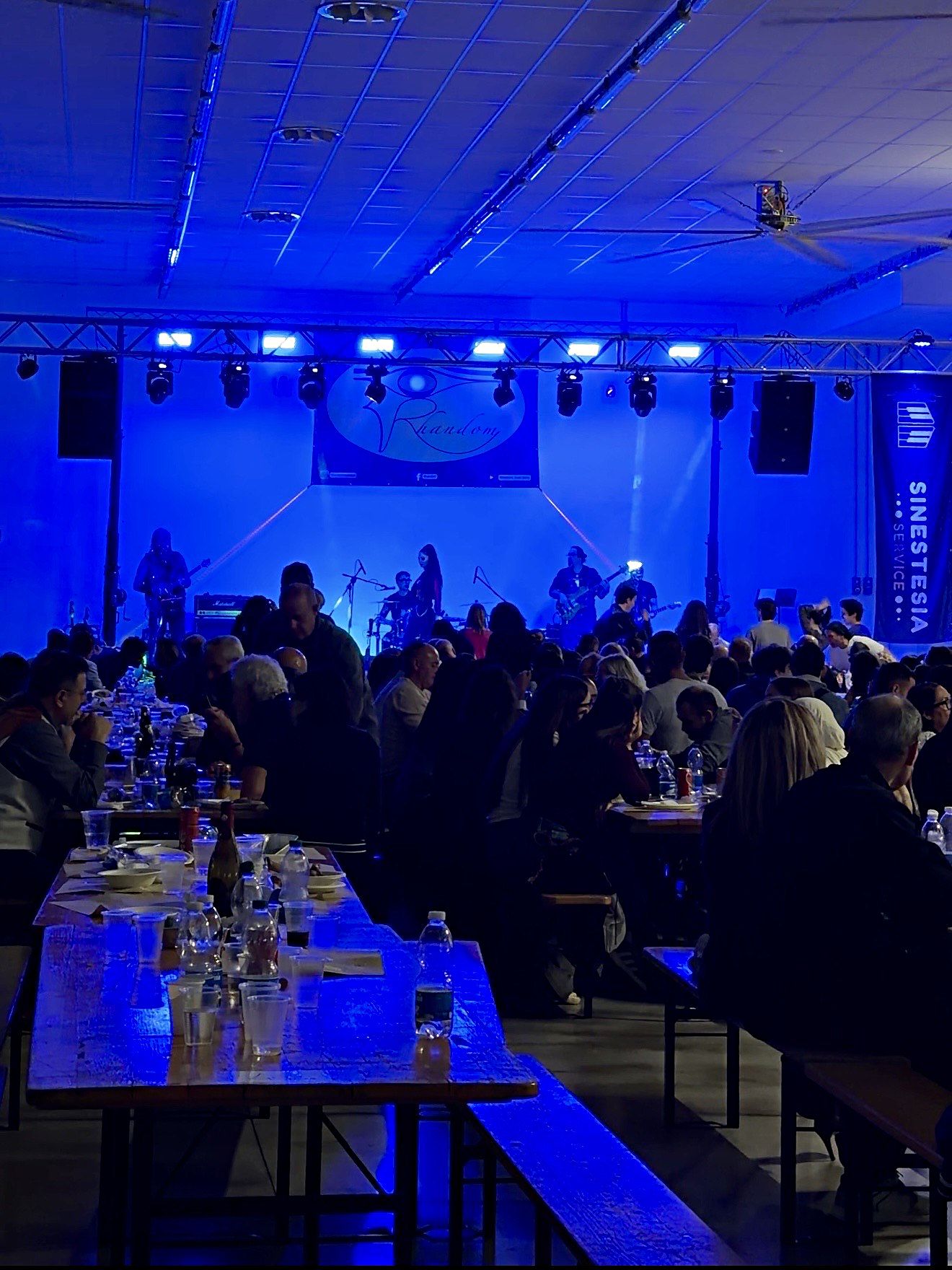 Una band suona sul palco del Palaspirà mentre il pubblico cena alle tavolate della sagra