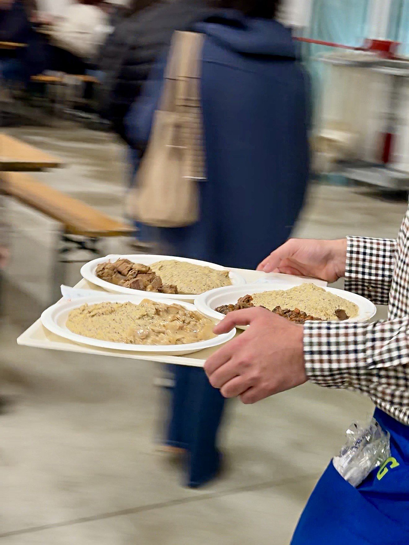 Un volontario porta ai tavoli un vassoio di piatti di polenta taragna con carne