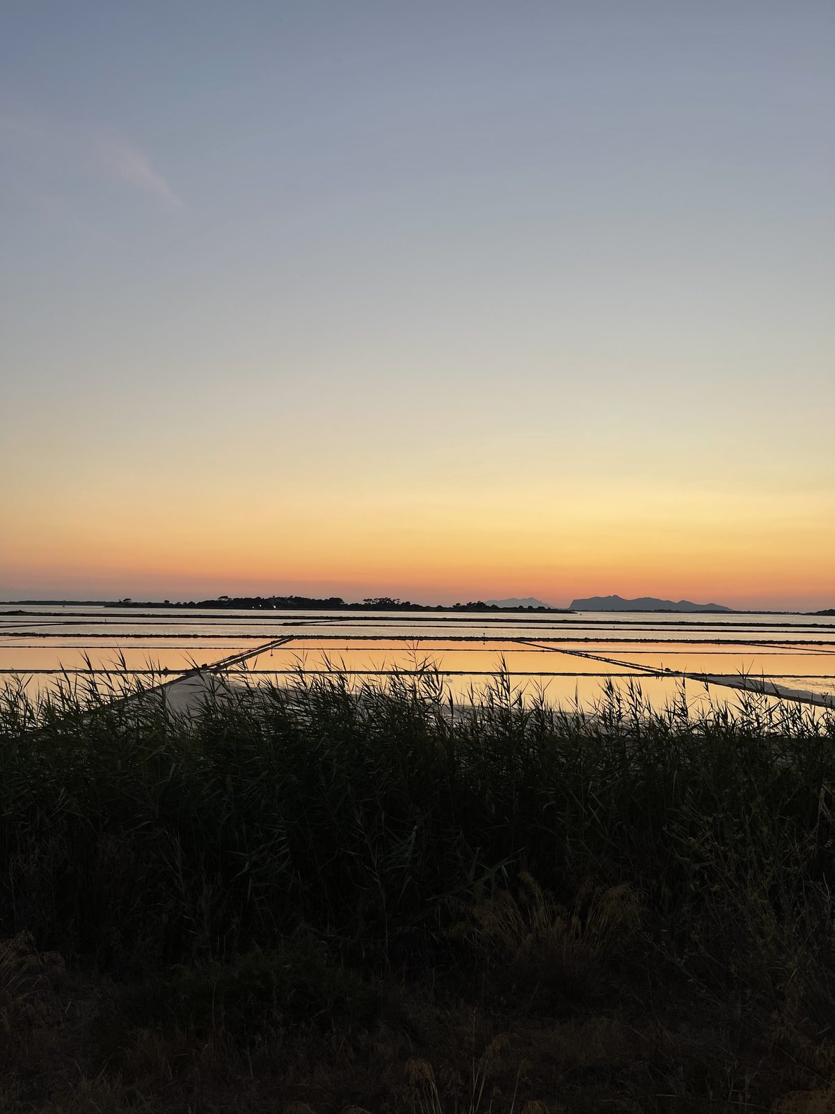 Le Saline di Marsala al tramonto, con i mulini a vento e i riflessi aranciati sull'acqua