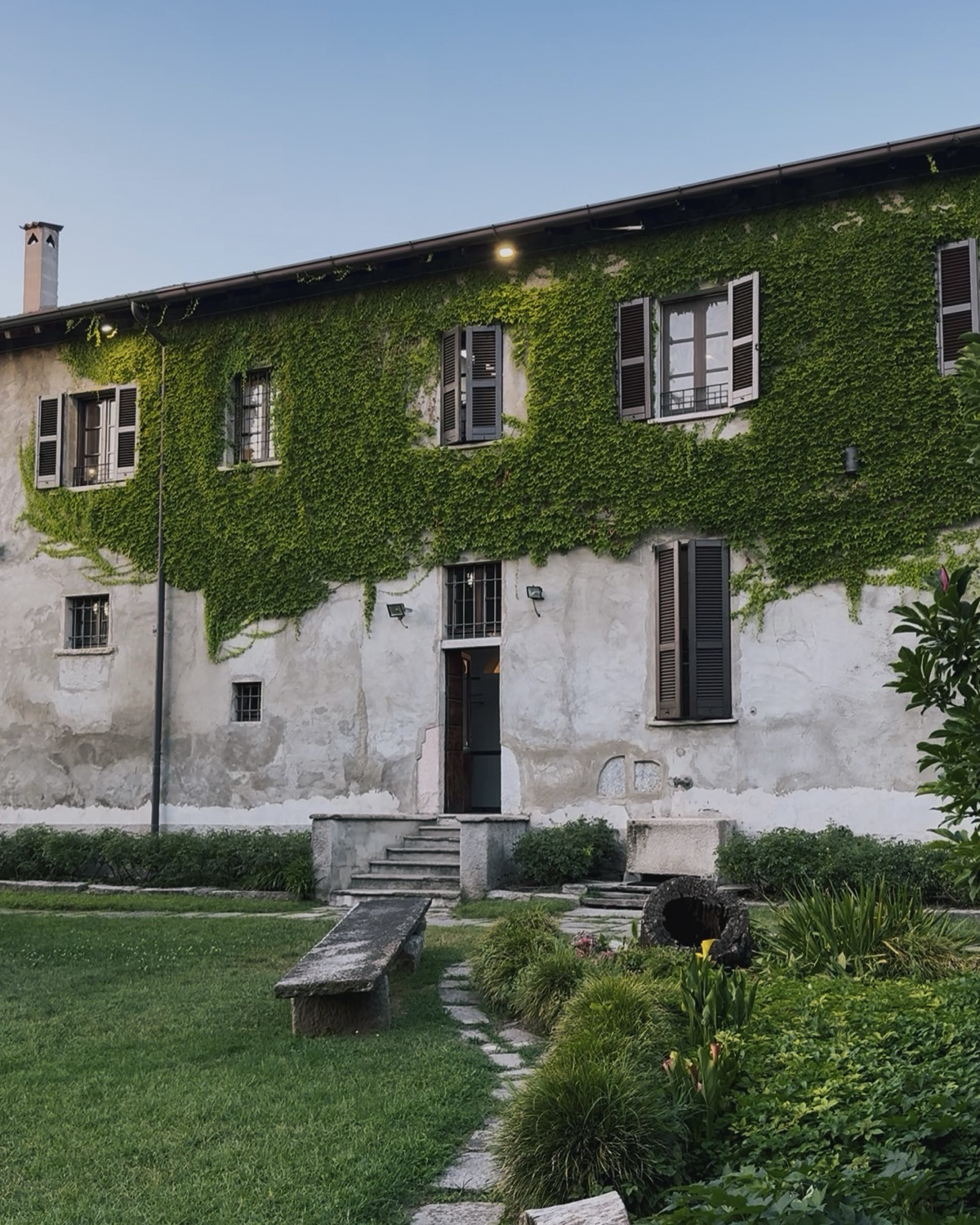 Facciata dell'Agriturismo Da Pippo a Cassignanica, cascina con muro coperto di edera, prato e panchina in pietra al tramonto