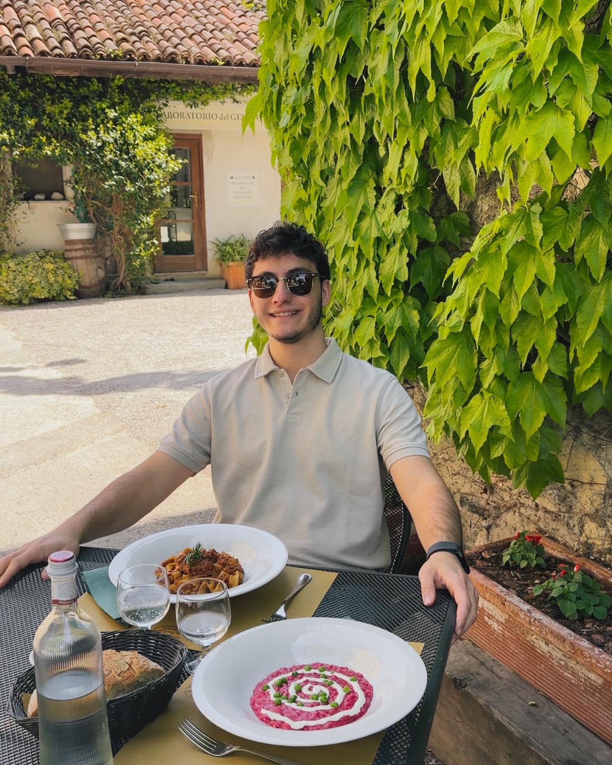 Gianmaria al tavolo esterno dell'Agriturismo Sant'Anna con il risotto alla barbabietola e la pasta al ragù, parete di edera alle spalle